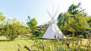 A white teepee in a grassy area with trees and a building in the background. - Bio-Hotel & Residence Kaufmann (Ora)