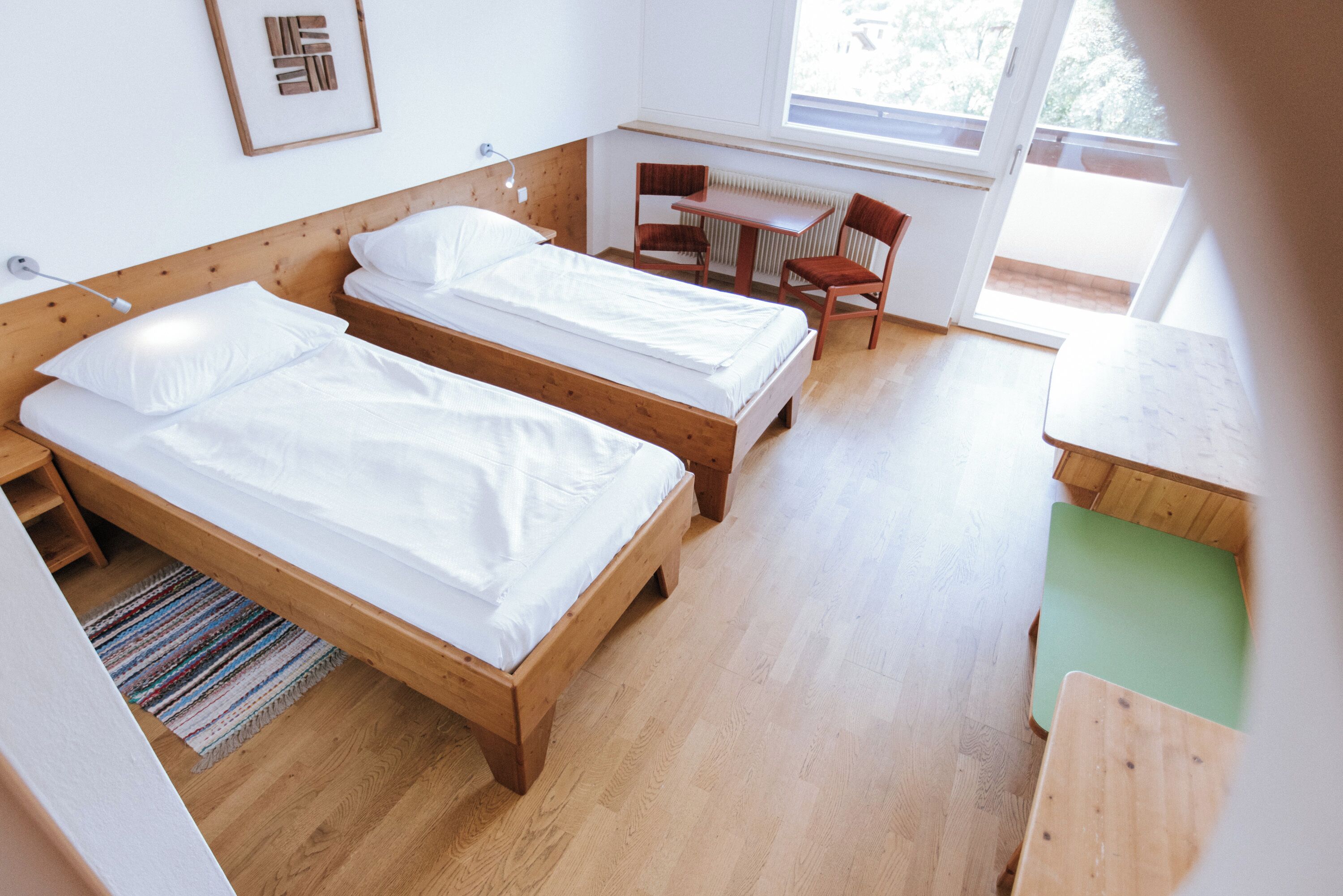 A room with two wooden beds, a desk, a chair, and a window.