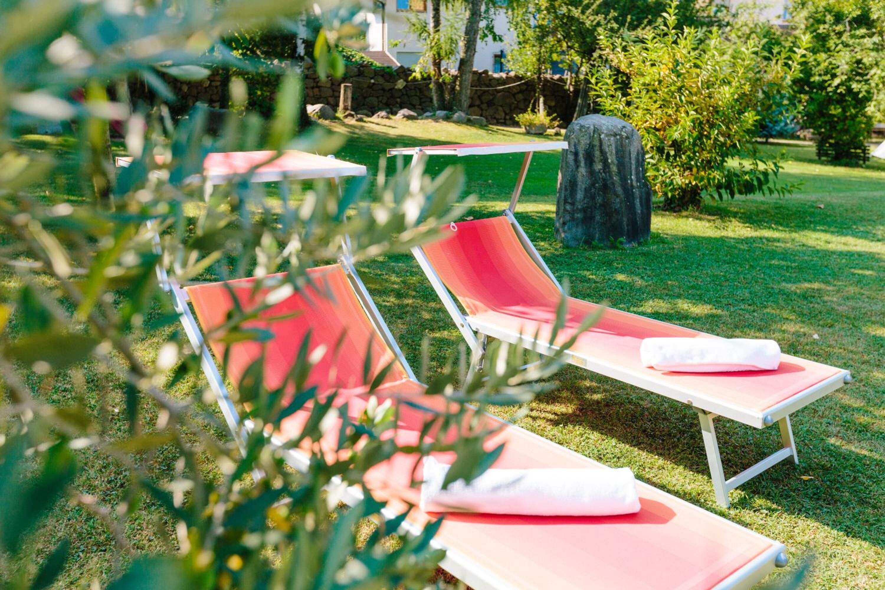 Two red lounge chairs with white cushions in a grassy outdoor area.