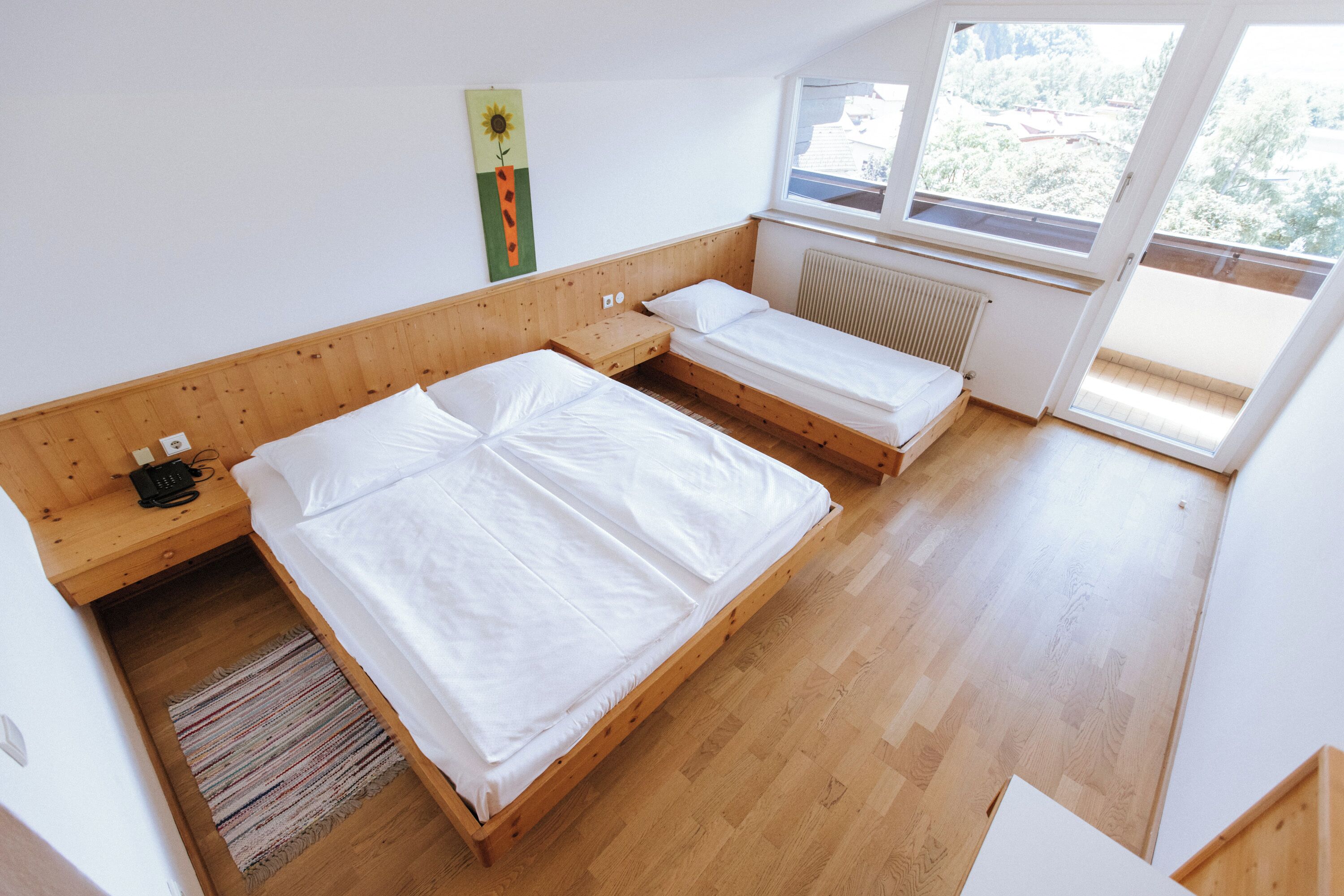 A bedroom with two single beds, a wooden headboard, a radiator, and a window with a view of greenery.