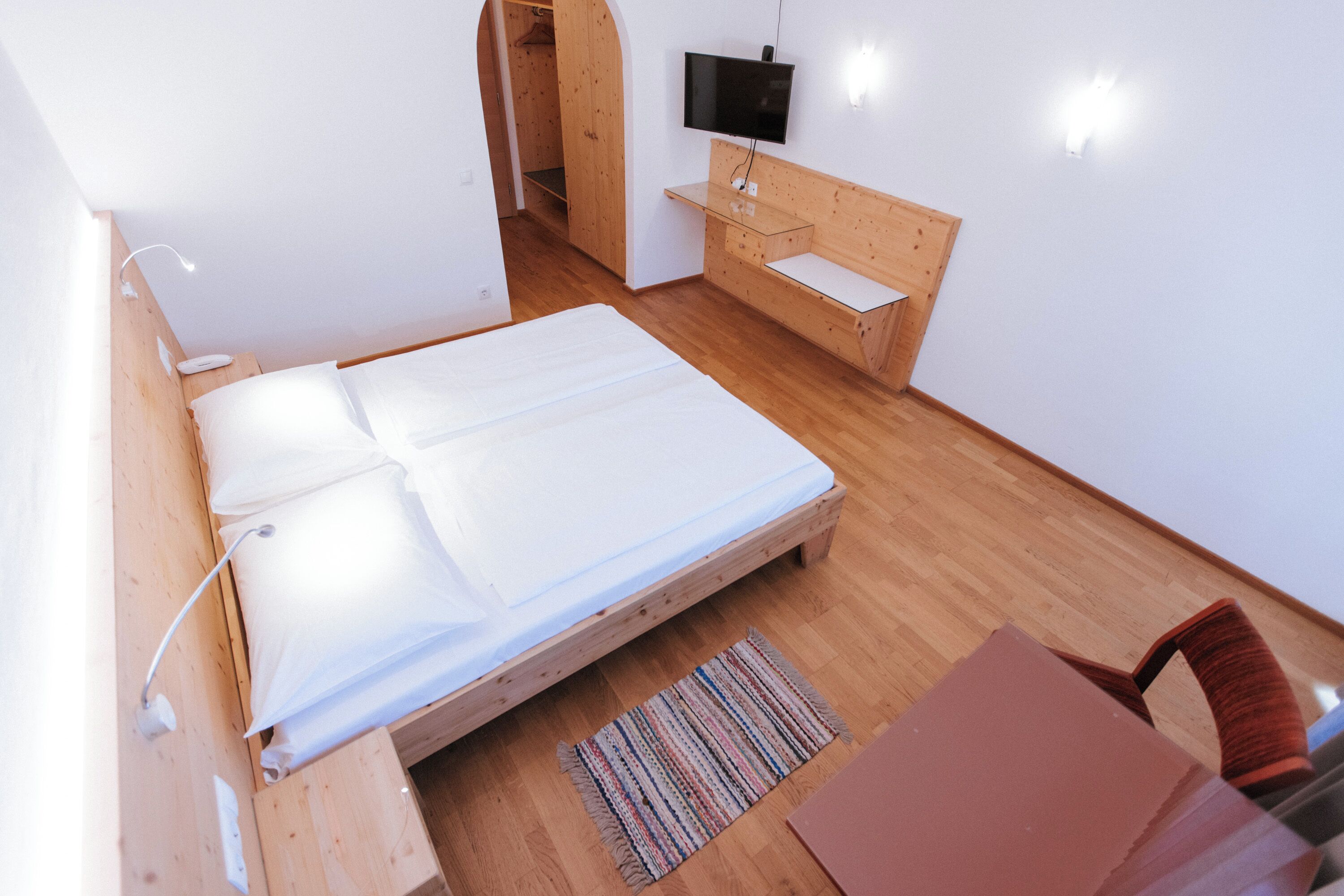 A bedroom with a wooden bed, a TV mounted on the wall, and a wooden desk.