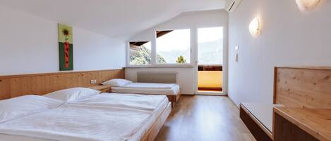 A bedroom with two beds, a wooden bench, a radiator, and a view of the outdoors.