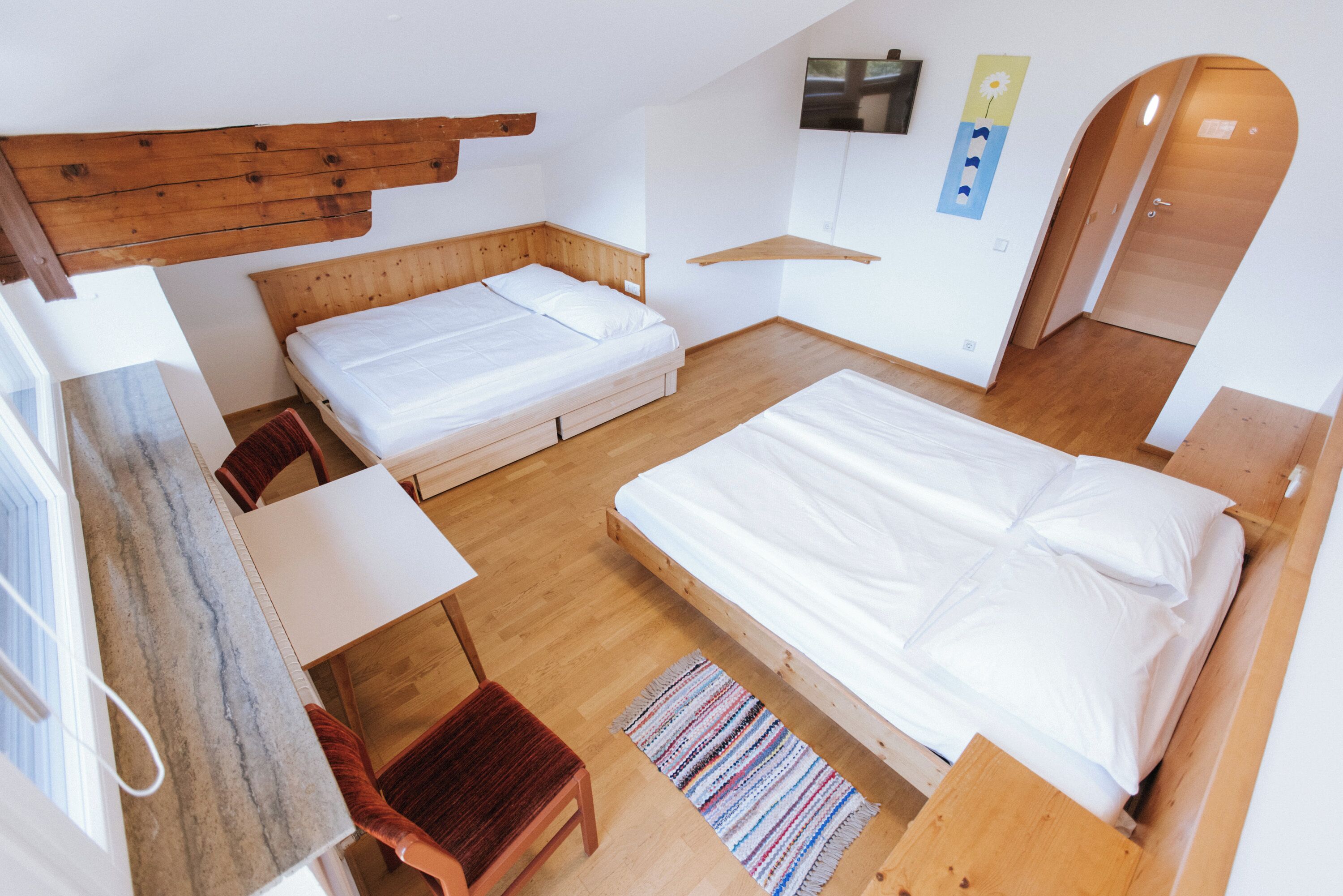 A room with two beds, a wooden headboard, a TV, and a wooden door.