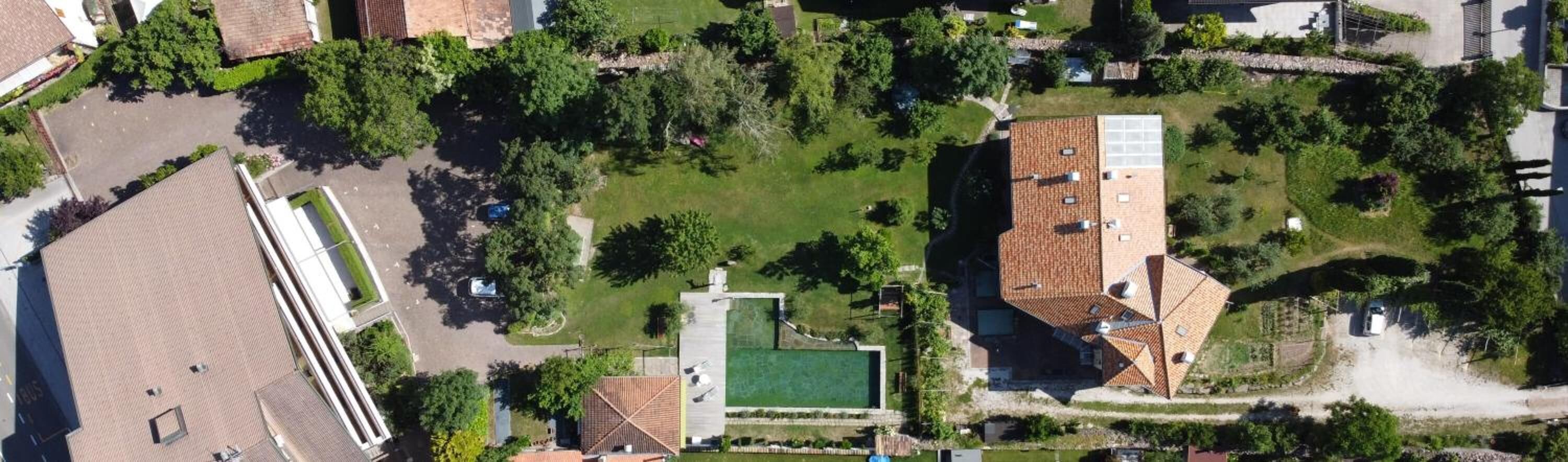 An aerial view of a residential area with a swimming pool, a tennis court, and a large house with a tiled roof.