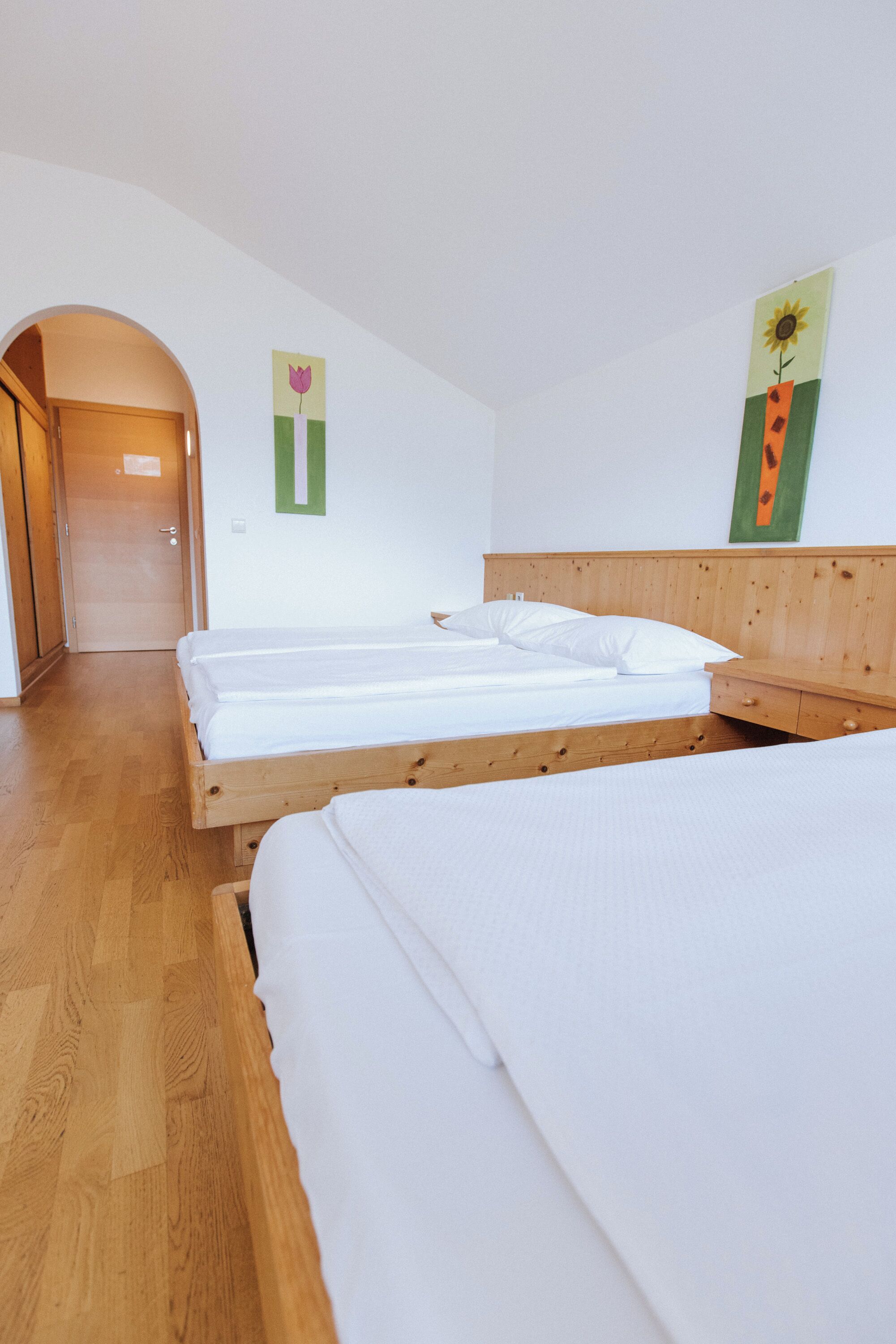 A room with two wooden beds, a wooden floor, a door, and a wall with a flower painting.
