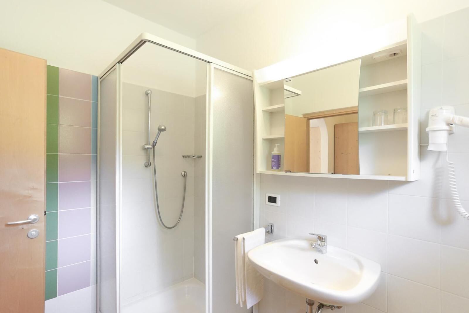 A modern bathroom with a glass-enclosed shower, a white sink, and a mirror above it.