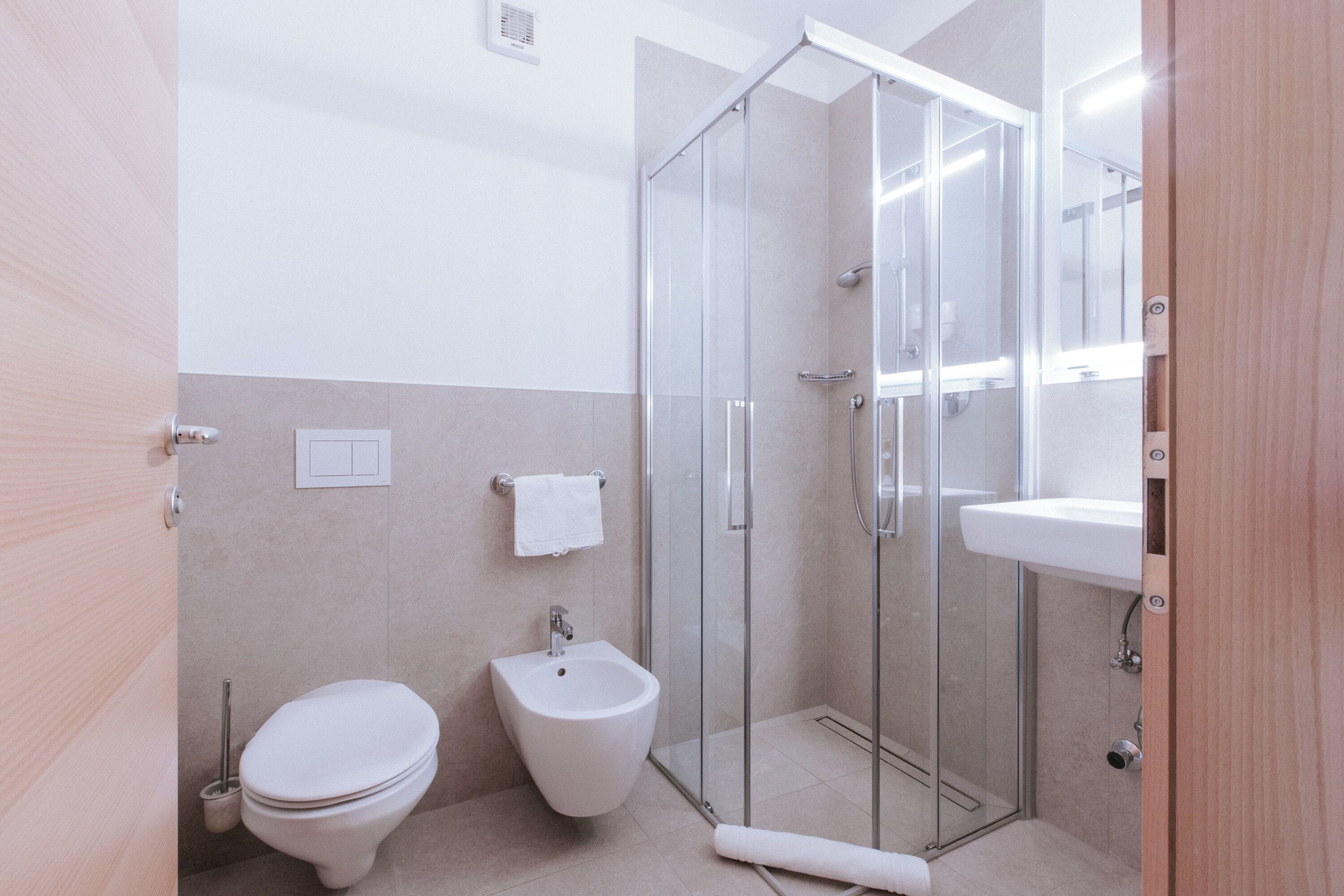 Et moderne badeværelse med toilet, bidet, glas brusekabine og håndvask.