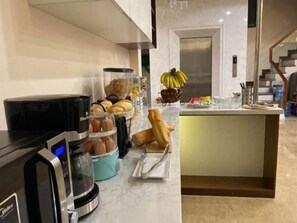Une cuisine moderne équipée d’une machine à café, d’un panier de fruits et d’une variété de produits de boulangerie.