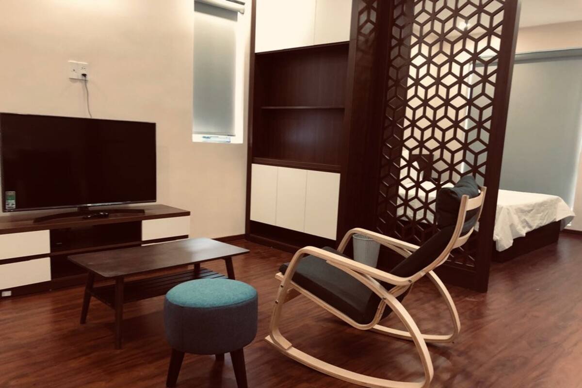 A modern living room with a flat-screen TV, a wooden coffee table, a rocking chair, a small ottoman, and a decorative partition with a geometric pattern.