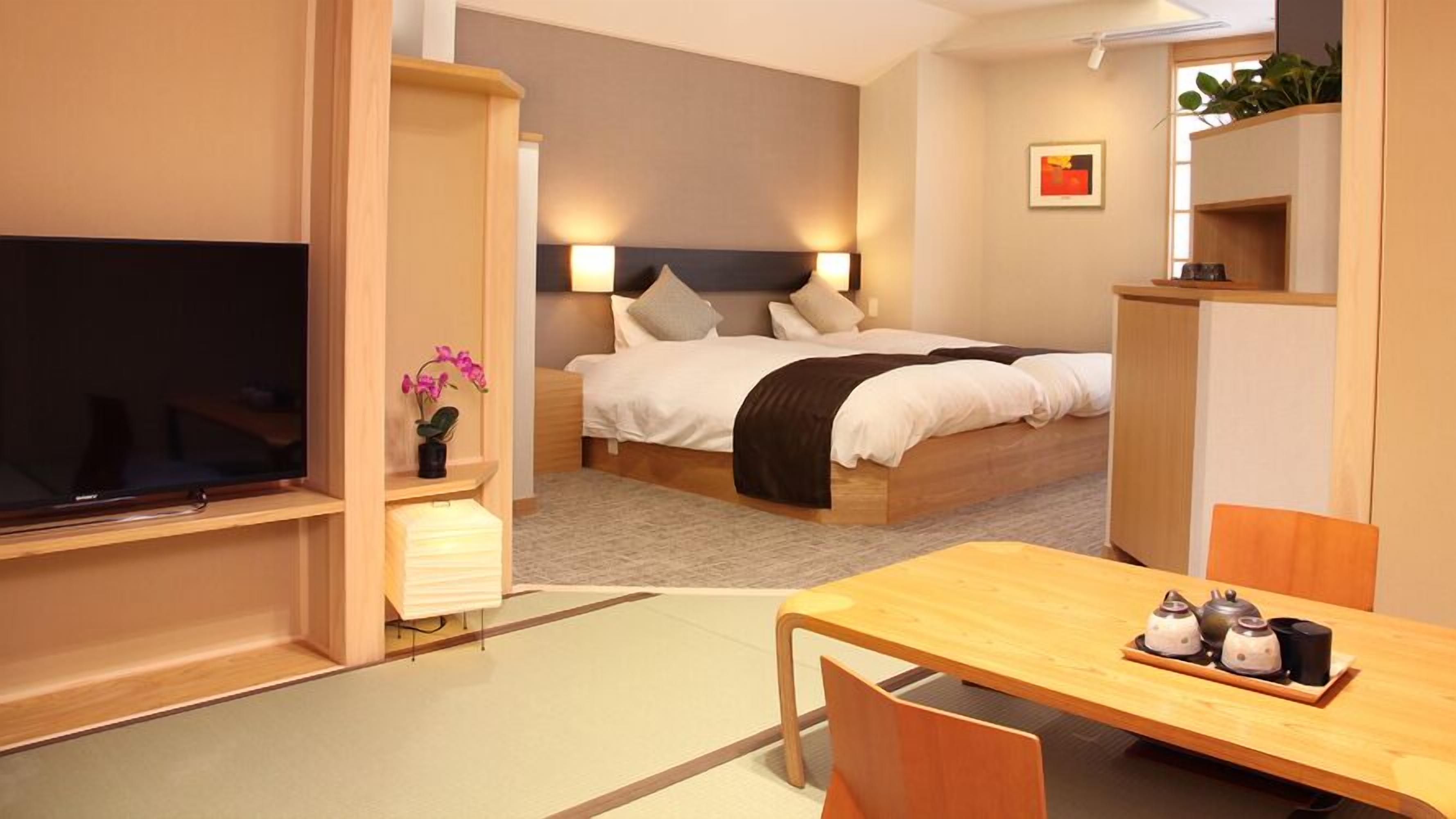 A hotel room with a bed, bedside table, TV, and a dining area with chairs and a table.