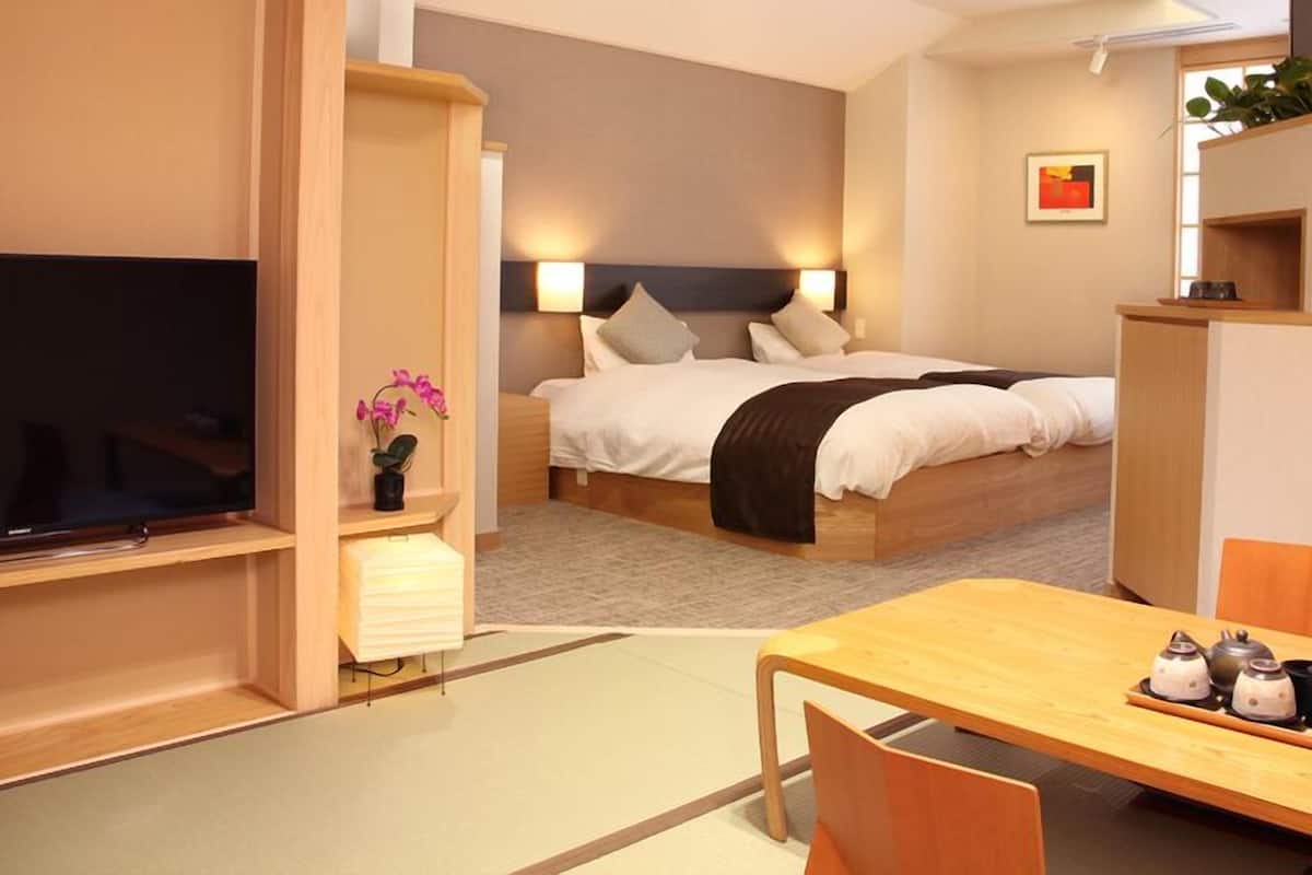 A hotel room with a bed, bedside table, TV, and a dining area with chairs and a table.