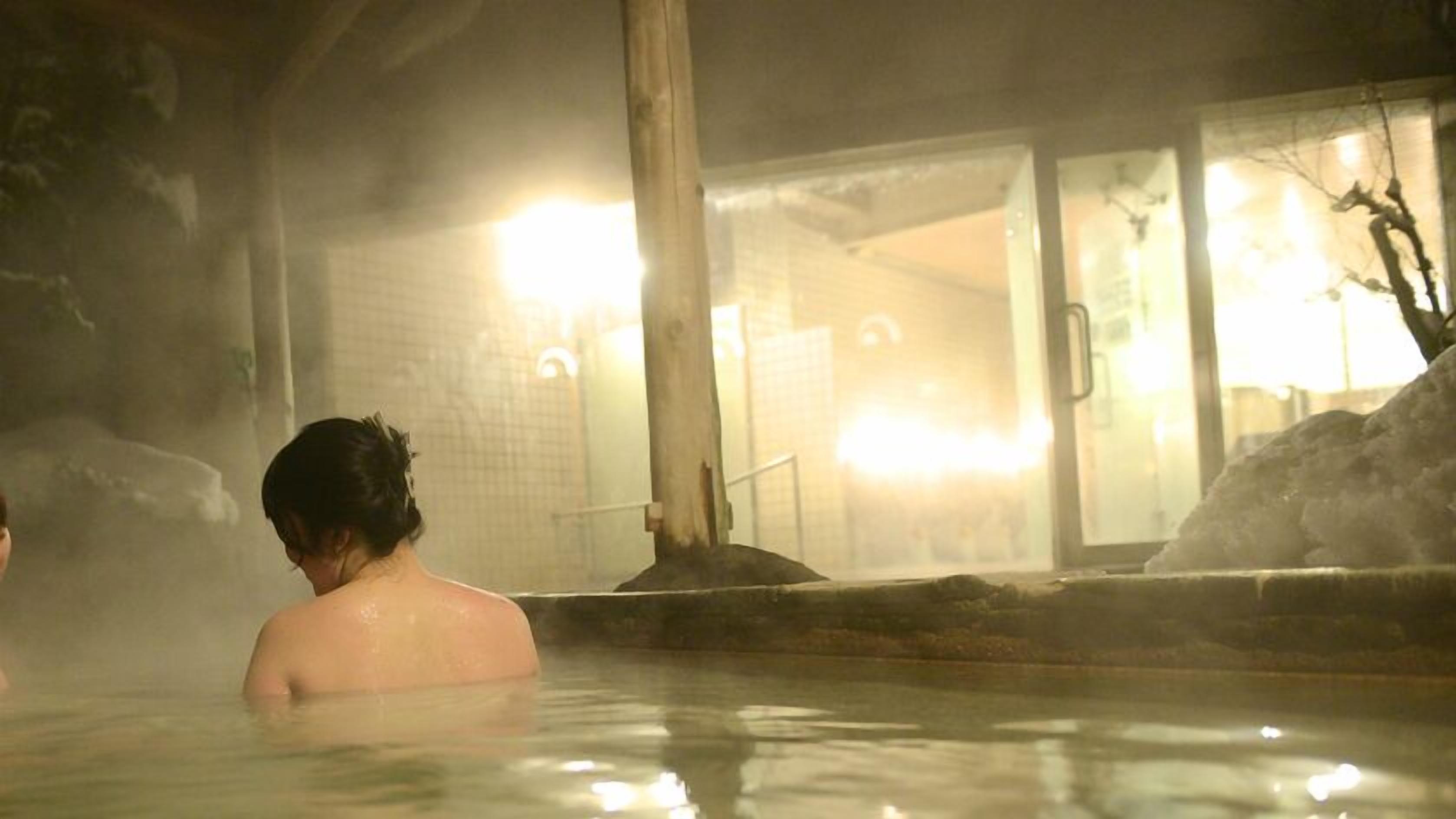 A person in a hot spring bath with a building in the background.