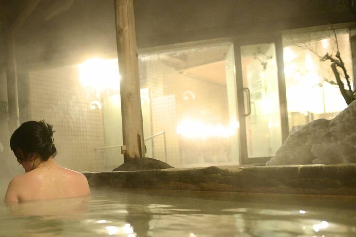 A person in a hot spring bath with a building in the background.