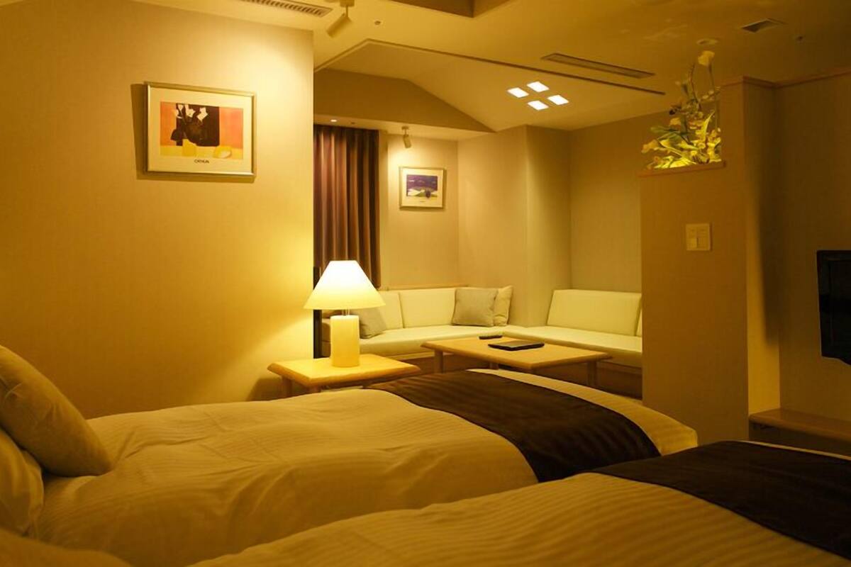 A hotel room with two beds, a sofa, a table, and a lamp.