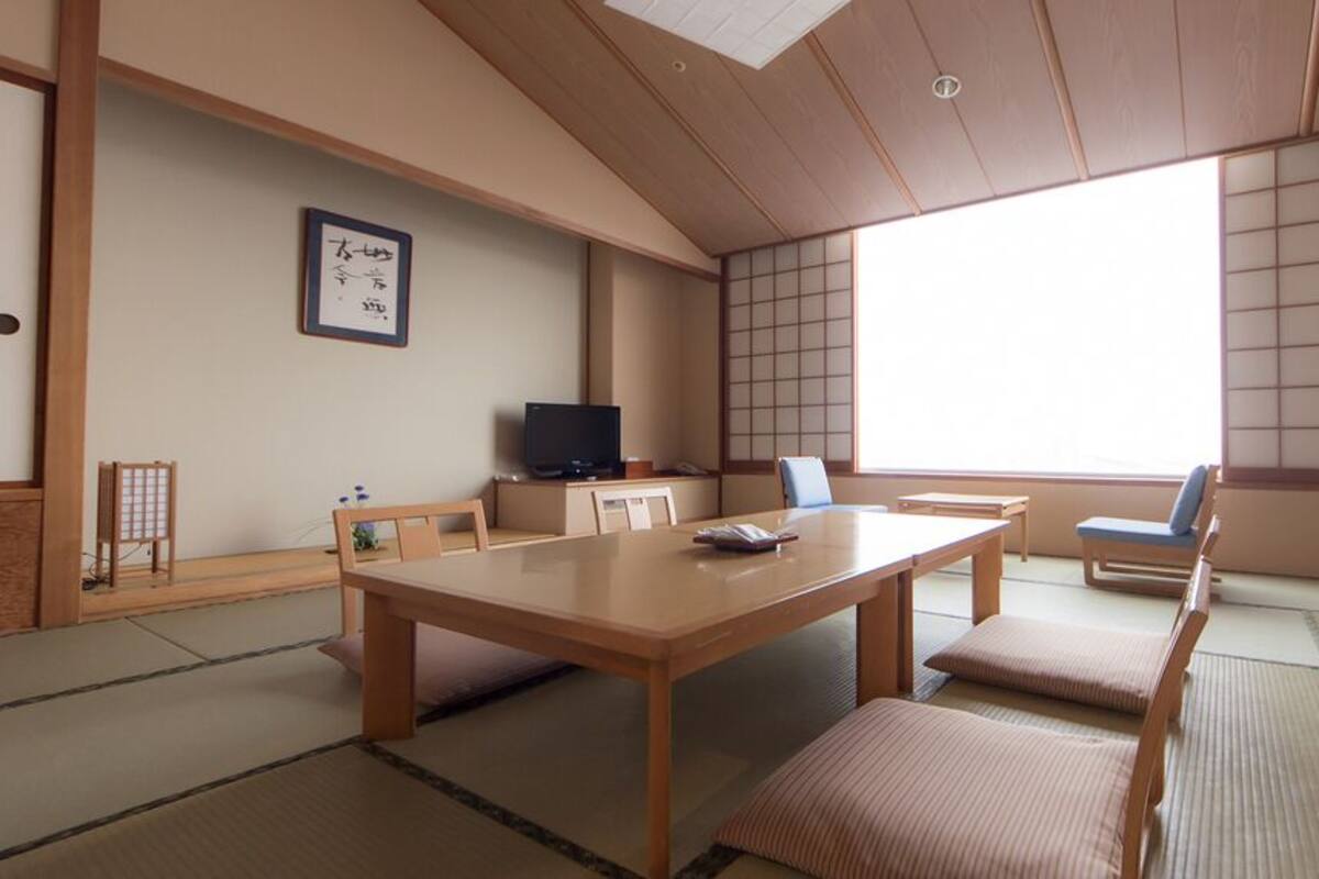 A traditional Japanese room with tatami flooring, a low table, a television, and a sliding door.