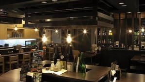 Un interior de restaurante con una mesa central, iluminación colgante y una zona de bar al fondo.