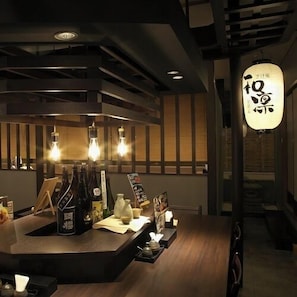 Ein Restaurantinneres mit einer Theke, hängenden Glühbirnen und einem traditionellen japanischen Laternenleuchter.