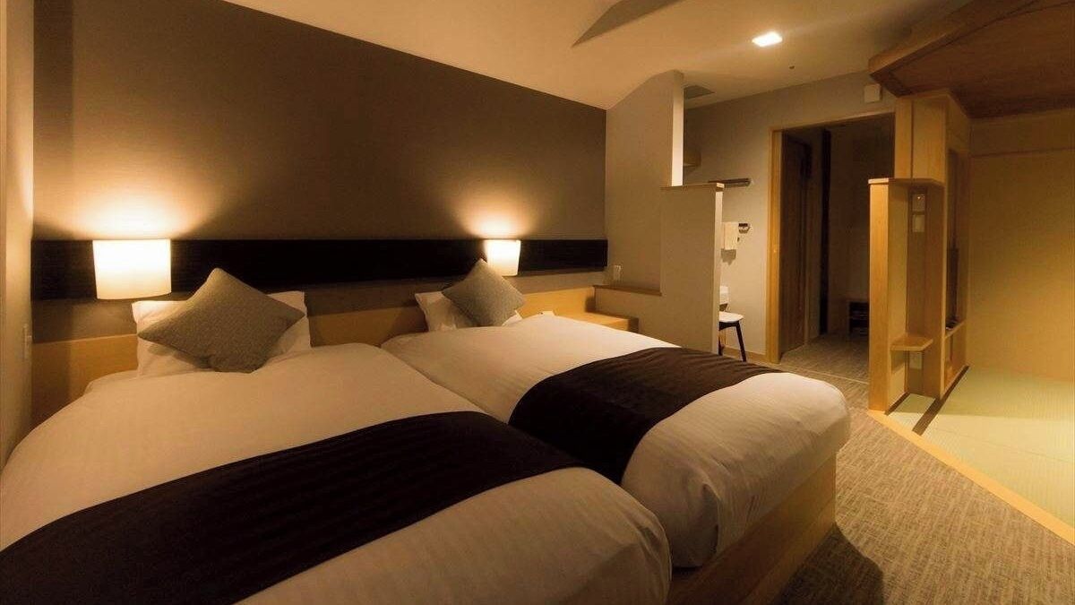 A hotel room with two beds, nightstands, a wooden wardrobe, and a small seating area.