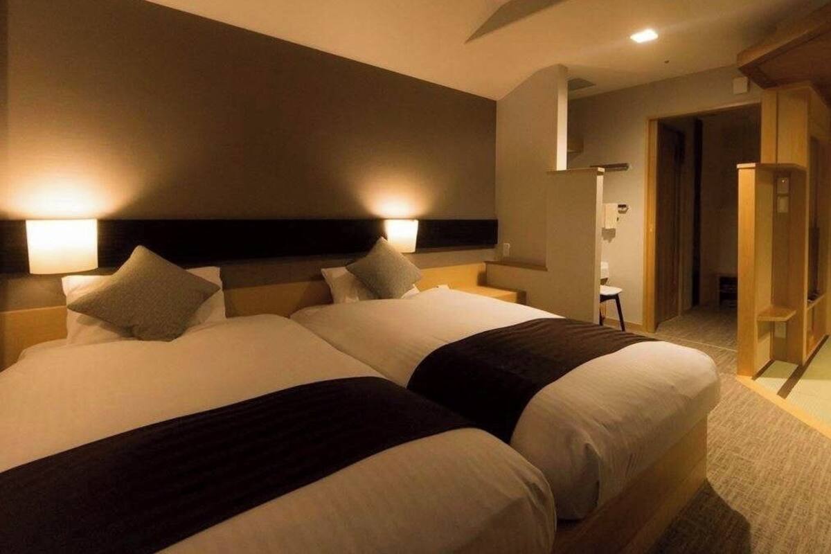 A hotel room with two beds, nightstands, a wooden wardrobe, and a small seating area.