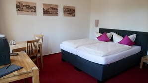 Ein Hotelzimmer mit Bett, Schreibtisch und Stühlen. An der Wand hängen drei gerahmte Bilder.