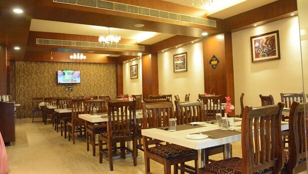 A dining area with wooden tables and chairs, a television mounted on the wall, and framed artwork on the walls. - Hotel Eden Roc (Bhubaneshwar)