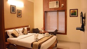 A hotel room with a large bed, a small table with chairs, a window with blinds, and a wall-mounted TV. - Hotel Eden Roc (Bhubaneshwar)
