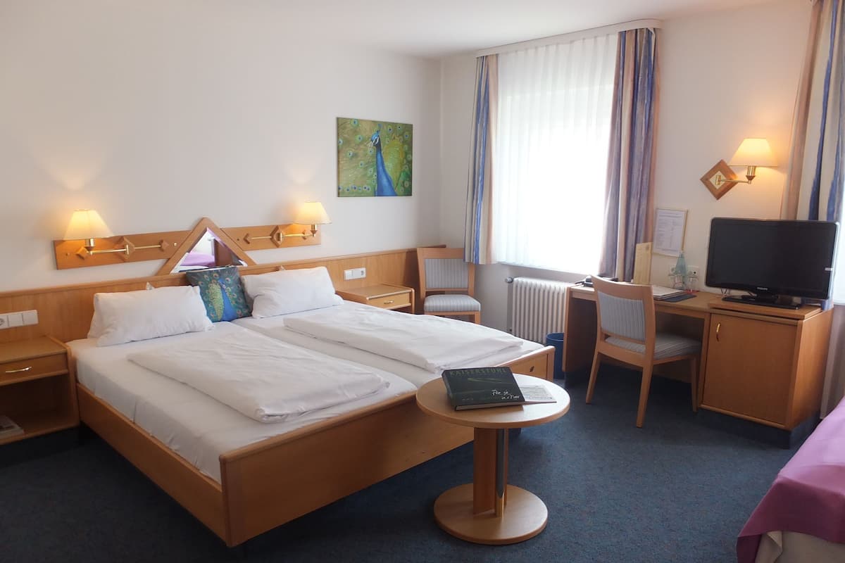 Habitación de hotel con una cama grande, mesitas de noche, un escritorio con silla, televisor y una ventana con cortinas.
