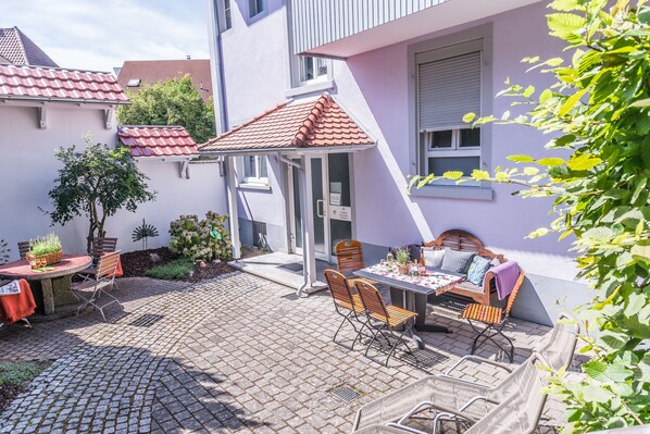 A patio with a table and chairs, a small garden, and a building with a red-tiled roof. - Hotel Pfauen (Endingen am Kaiserstuhl)