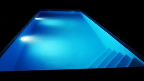 Una piscina larga y estrecha con iluminación azul en su interior y una serie de escalones para entrar.