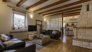 Una sala de estar con un sofá, una mesa de centro y una chimenea. Hay un televisor montado en la pared y una ventana con cortinas decorativas.