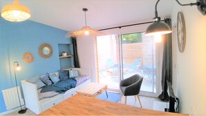 A cozy room with a blue wall, a white sofa, a wooden table, and a black chair. There are two pendant lights and a large window with a view of the outside. - House for 4 travelers, with private courtyard - between the city center and the port (Saint-Brieuc)