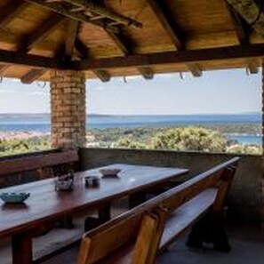 An outdoor patio with a wooden table and benches, overlooking a scenic landscape. - Apartments Lidija (Rab)