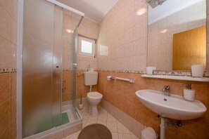 A bathroom with a glass-enclosed shower, a toilet, a sink, and a mirror. - Apartments Lidija (Rab)