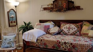 Un dormitorio con una cama de madera, una mecedora, una lámpara, un reloj de pared y un pequeño adorno de cabaña de madera.