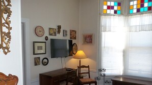 Una sala de estar con un escritorio de madera, sillas, un televisor y varias decoraciones en las paredes.