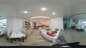 A dining area with round tables, a buffet with various food items, and a view of the outside through large windows. - Hotel Minas (Tres Marias)