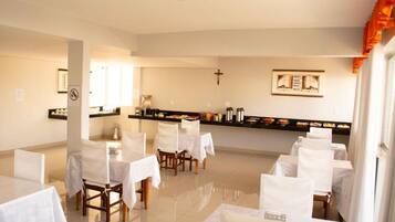 Uma área de refeições com mesas preparadas para o serviço, um balcão de buffet e uma cruz na parede.