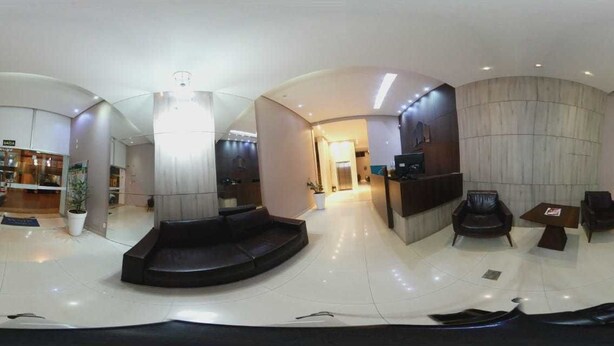 A modern hotel lobby with a reception desk, seating area, and a large potted plant. - Hotel Minas (Tres Marias)