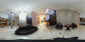 A modern hotel lobby with a reception desk, seating area, and a large potted plant.