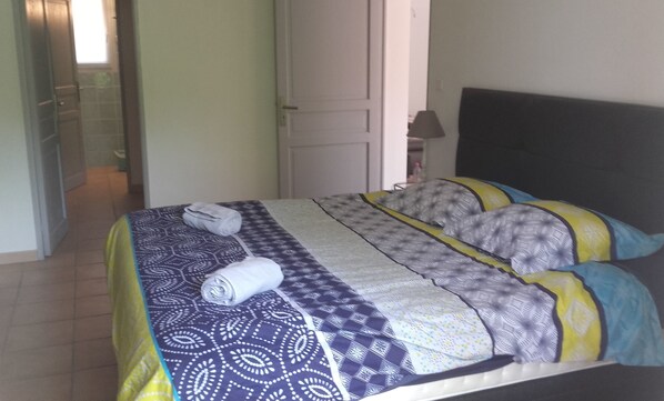 A bed with patterned bedding, a rolled towel, and a nightstand with a lamp. - La Lavande Bleue (Le Luc)