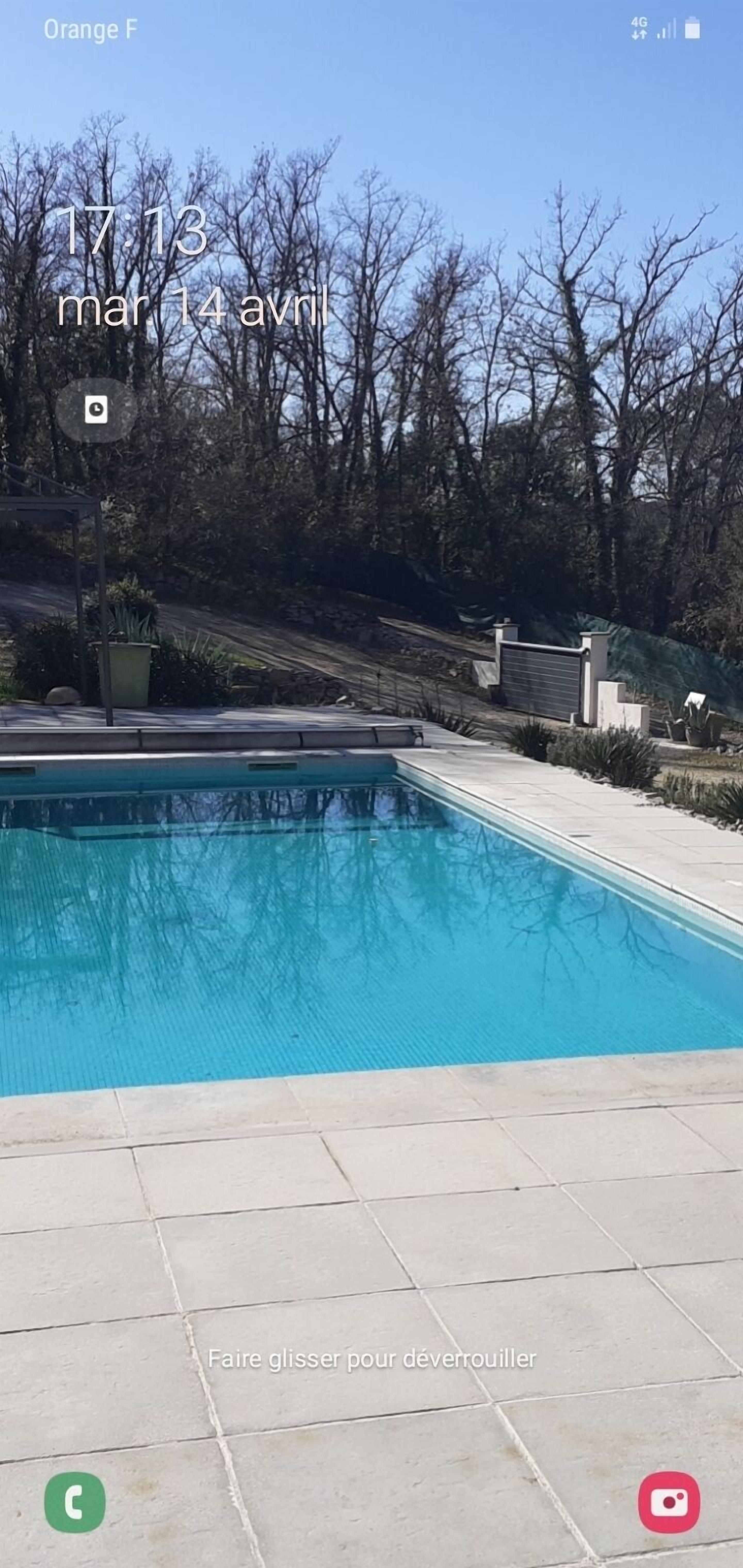 A swimming pool with a tiled deck, surrounded by trees and a gate.