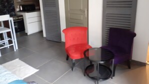 Una habitación pequeña y moderna con kitchenette, una silla roja, una silla morada y una mesa de vidrio.
