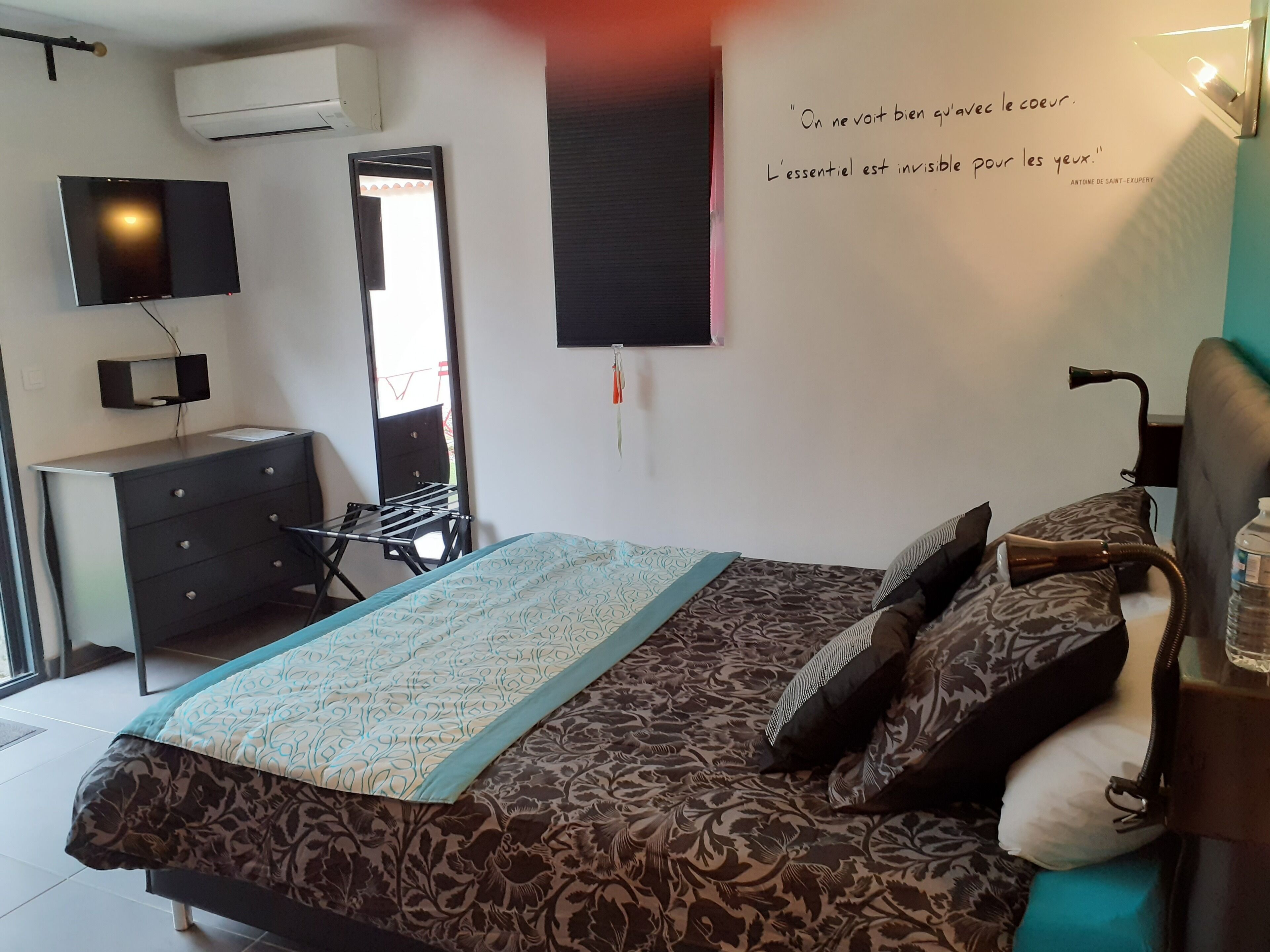 Un dormitorio con cama, cómoda, espejo, televisor montado en la pared y una cita en la pared.