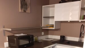Cocina compacta con microondas, estufa y muebles blancos.
