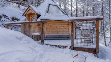 A wooden cabin with a snow-covered roof, surrounded by a wooden fence and snow-covered ground.