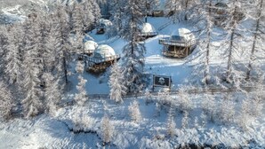 Zona montañosa nevada con varias construcciones de forma abovedada, probablemente alojamientos, rodeada de árboles y un cielo despejado.