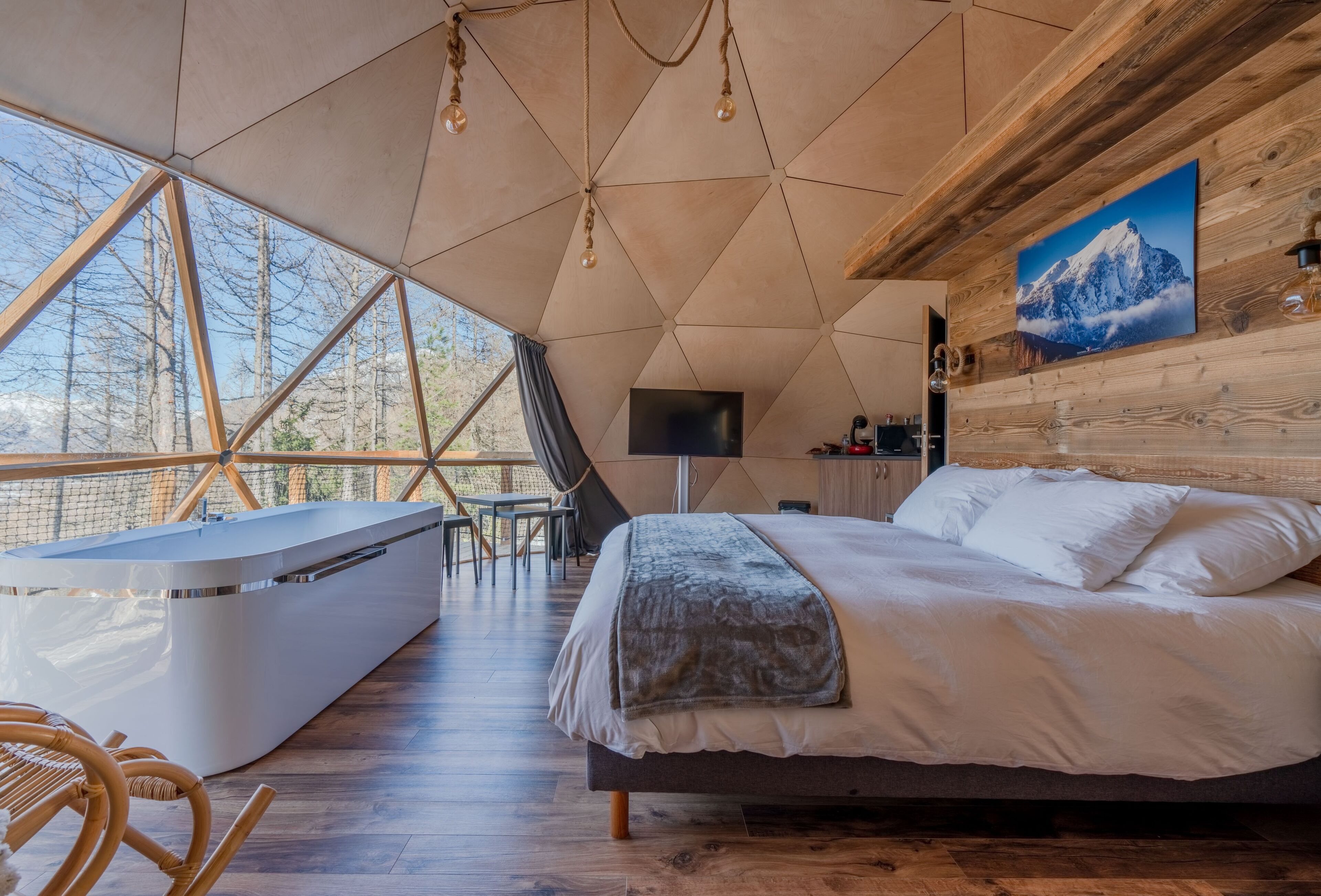 A modern bedroom with a large bed, a seating area with a sofa and chairs, and a view of the outdoors through large windows.