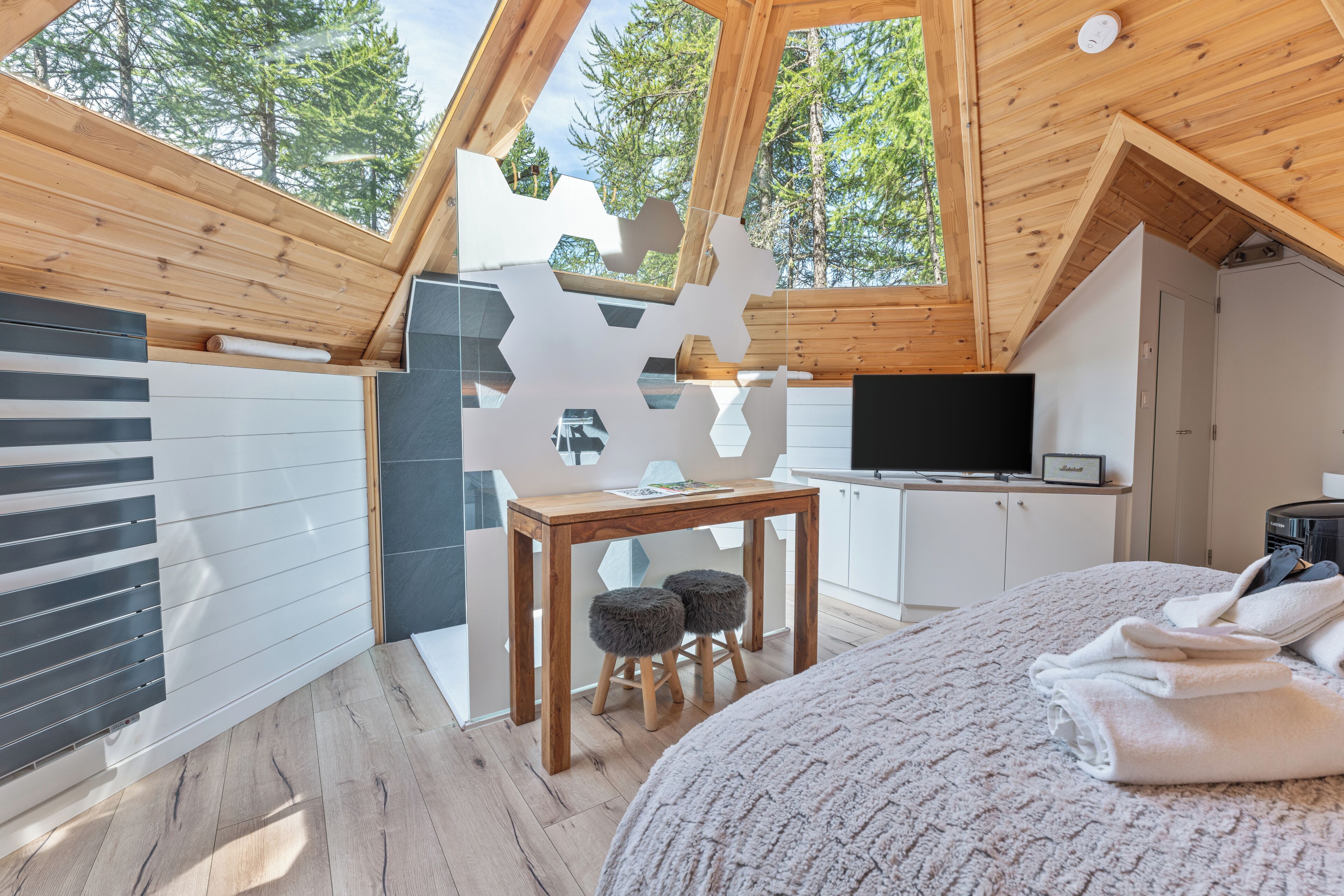 Une chambre moderne avec un plafond en pente, un lit, une télévision et une petite table avec des tabourets.