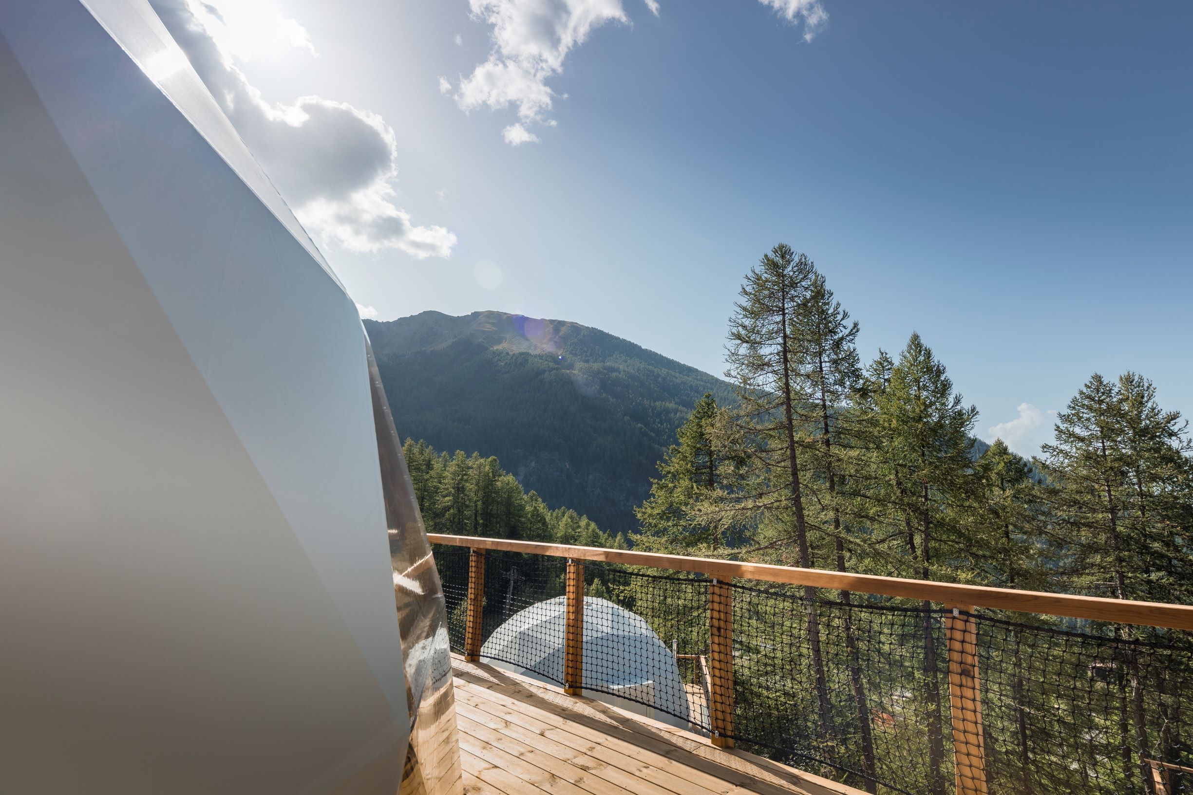 A balcony with a wooden railing overlooking a mountainous landscape with dense forest.