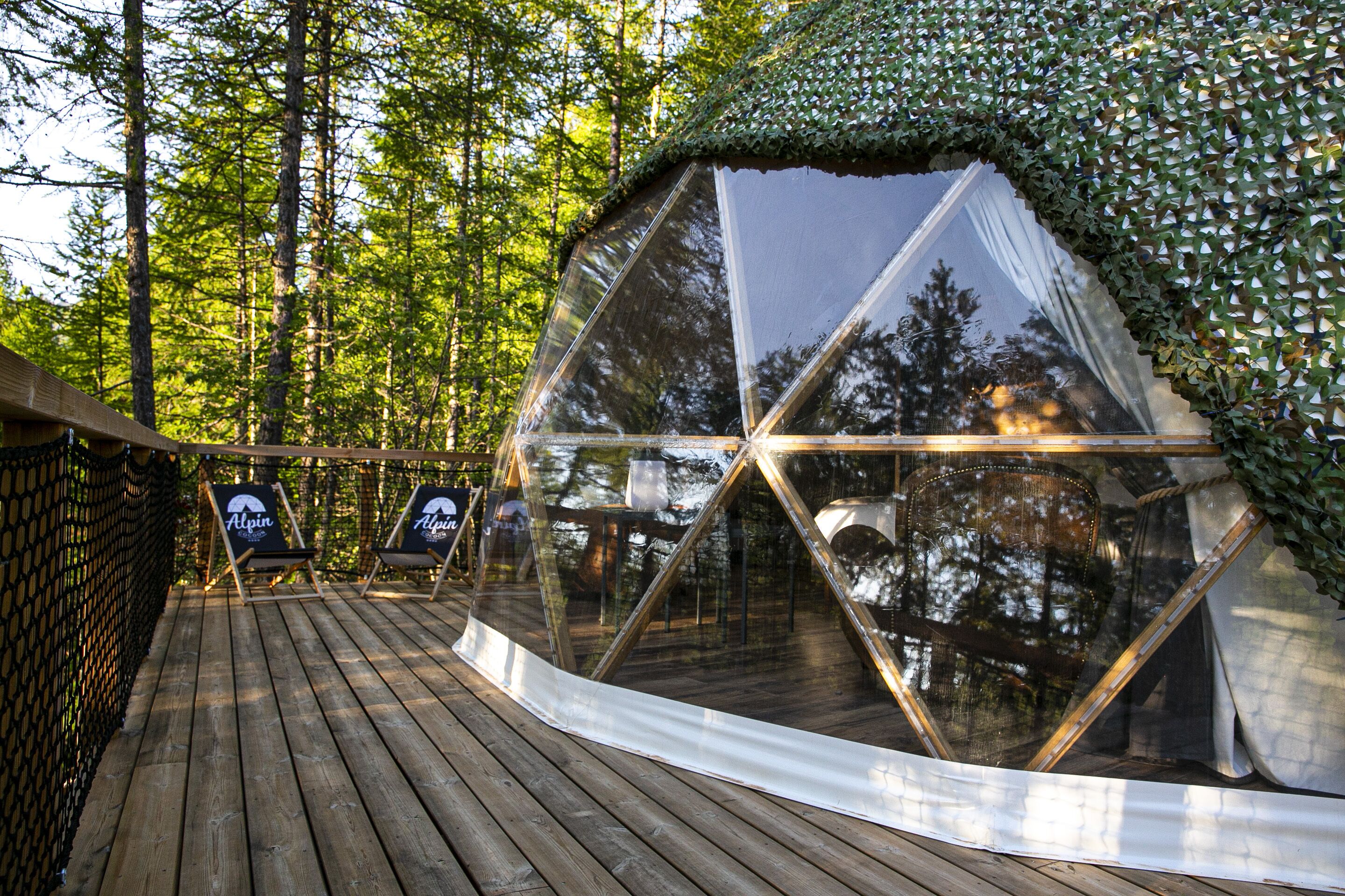 Una estructura de domo geodésico con una terraza de madera y dos sillones.
